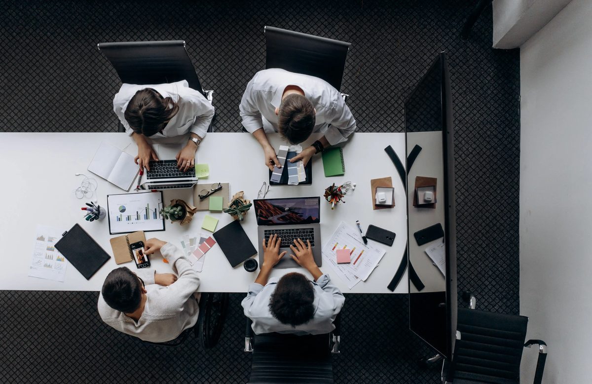 A team working across laptops, tablets and printed notes at a shared table